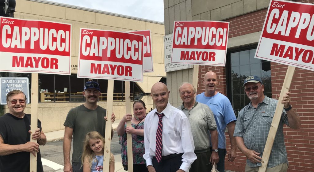 Bob Cappucci posing for a photo on a street corner with supporters holding signs